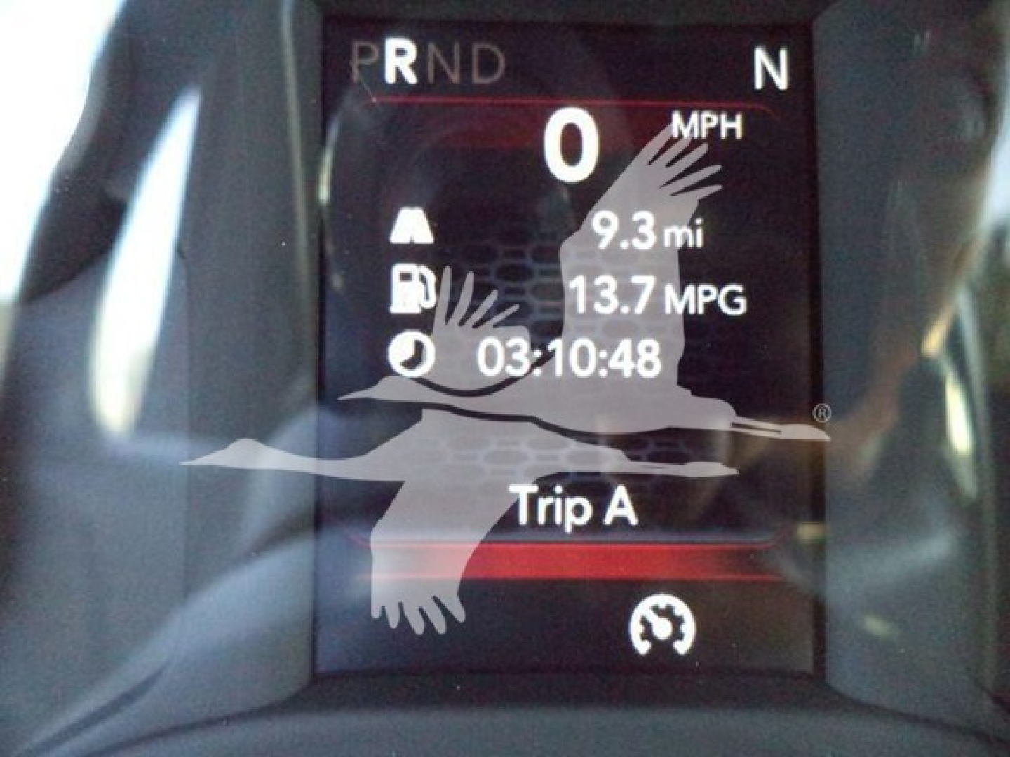 Vehicle gauge cluster showing 0 MPH, gear indicator PRNDNT, trip readout 9.3 mi, 13.7 MPG, 03:10:48, with a watermark image overlay.