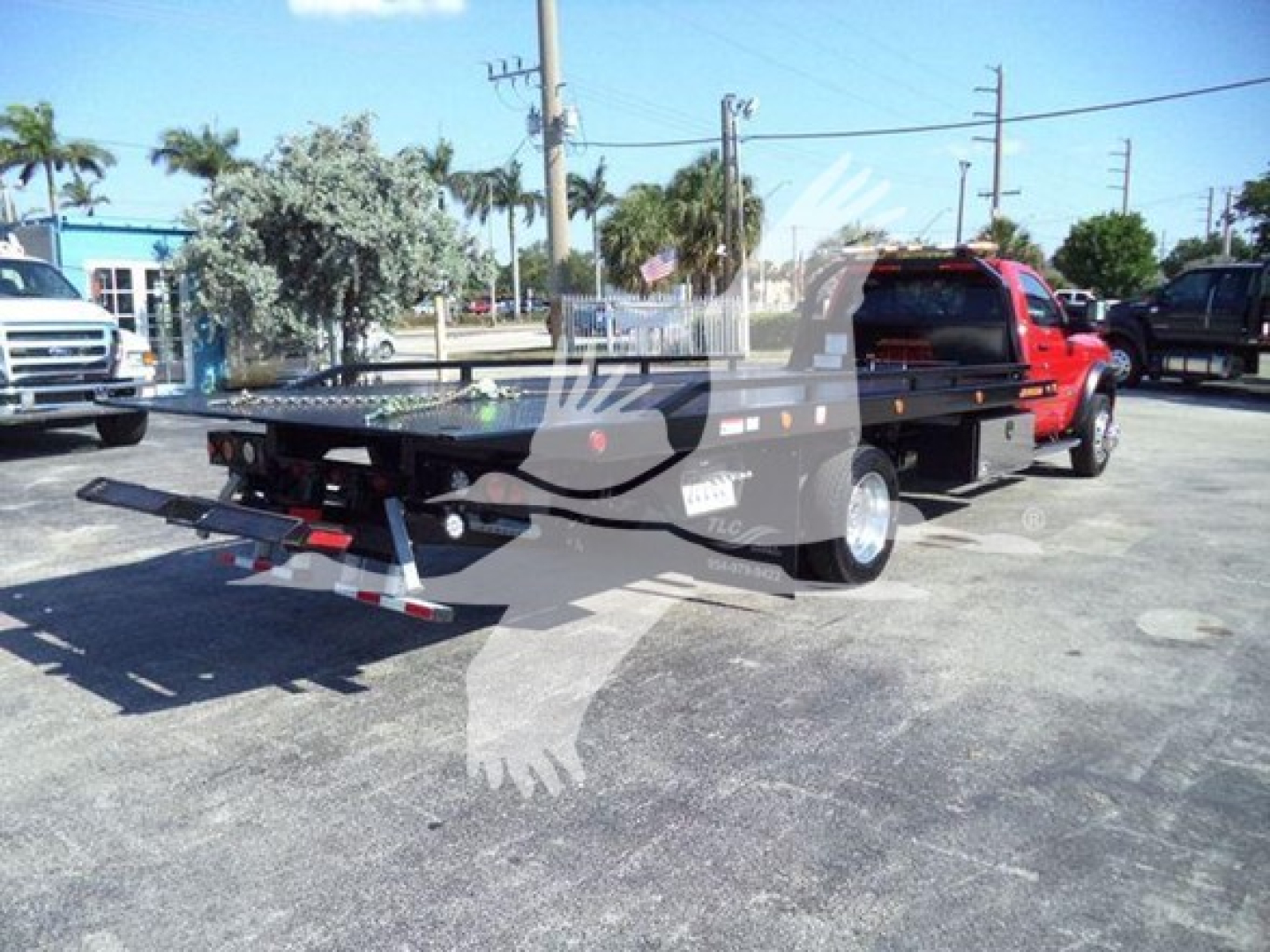 Ram 5500 rollback tow truck flatbed with black bed and red cab, side view showing rear equipment and hitch.