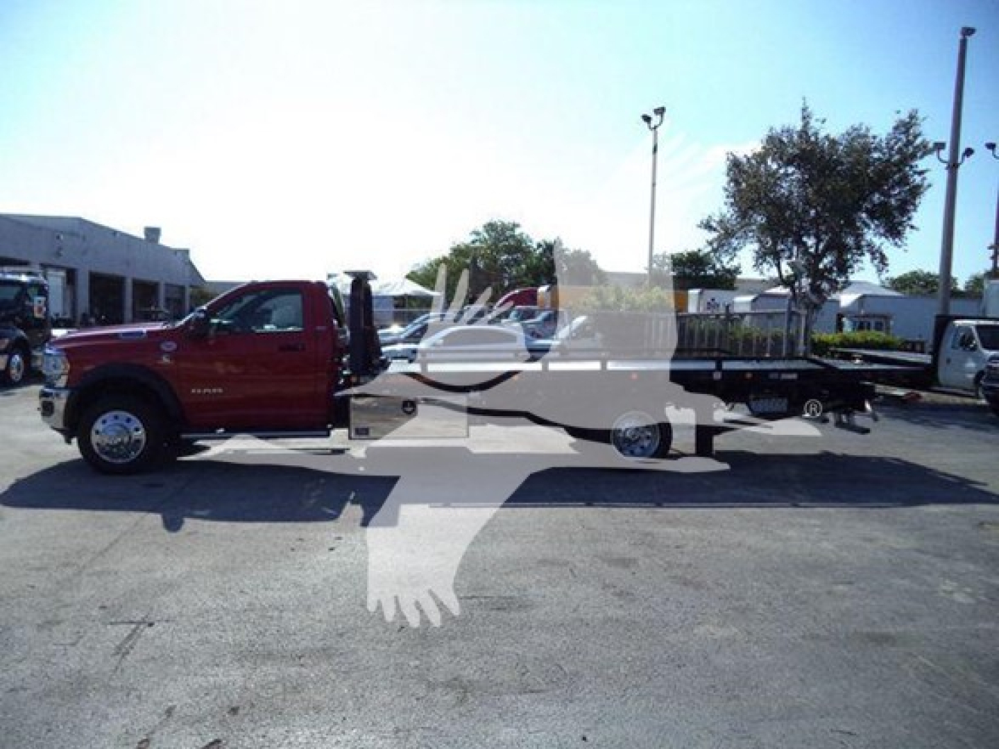 Ram 5500 rollback tow truck in a parking lot, side view, red cab with flatbed, no visible text readable on decals.