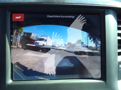 Truck rear view camera display showing a parking lot with a white truck and other vehicles; overlay graphic of hands on screen.