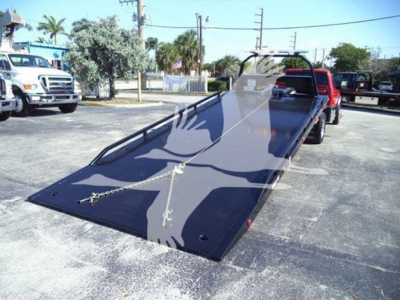 Ram 5500 rollback truck with a lowered flatbed in a parking lot showing a long black steel ramp and rear cab area.