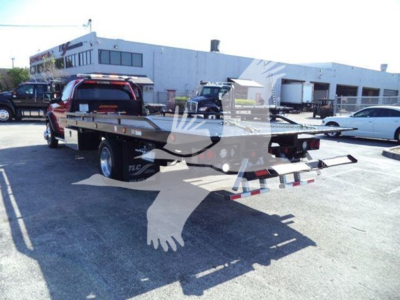 Ram 5500 rollback tow truck with flatbed, rear view showing ramps and platform, dealership lot in background.