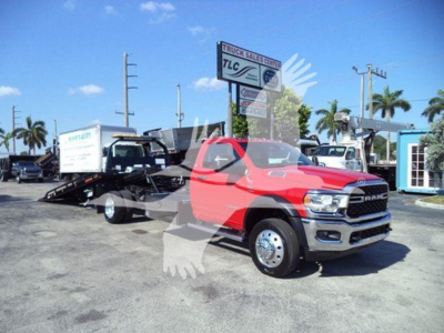 Ram 5500 SLT pickup in red with chrome bumper, shown parked in lot with rollback tow truck in background and dealership sign.