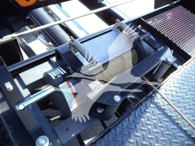 Winch assembly with steel cable on a Ram 5500 rollback truck, mounted on a diamond plate platform, hydraulic/rope winch visible with springs and mounting brackets.