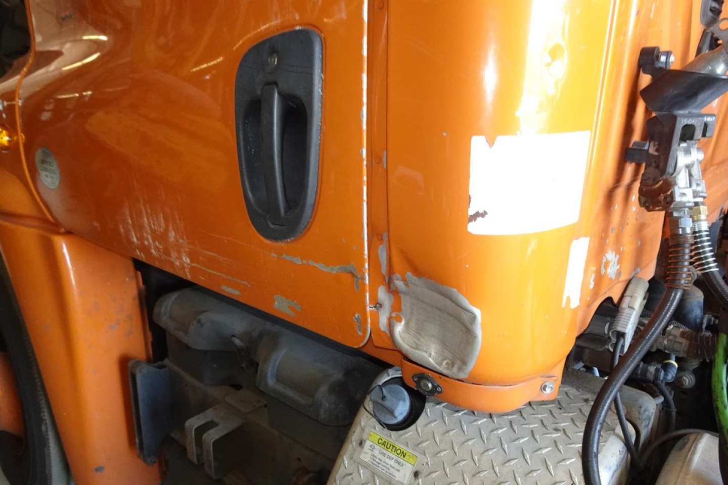 Cab portion of a Freightliner Cascadia 125 engine bay with orange paint and a warning label on the diamond plate step.