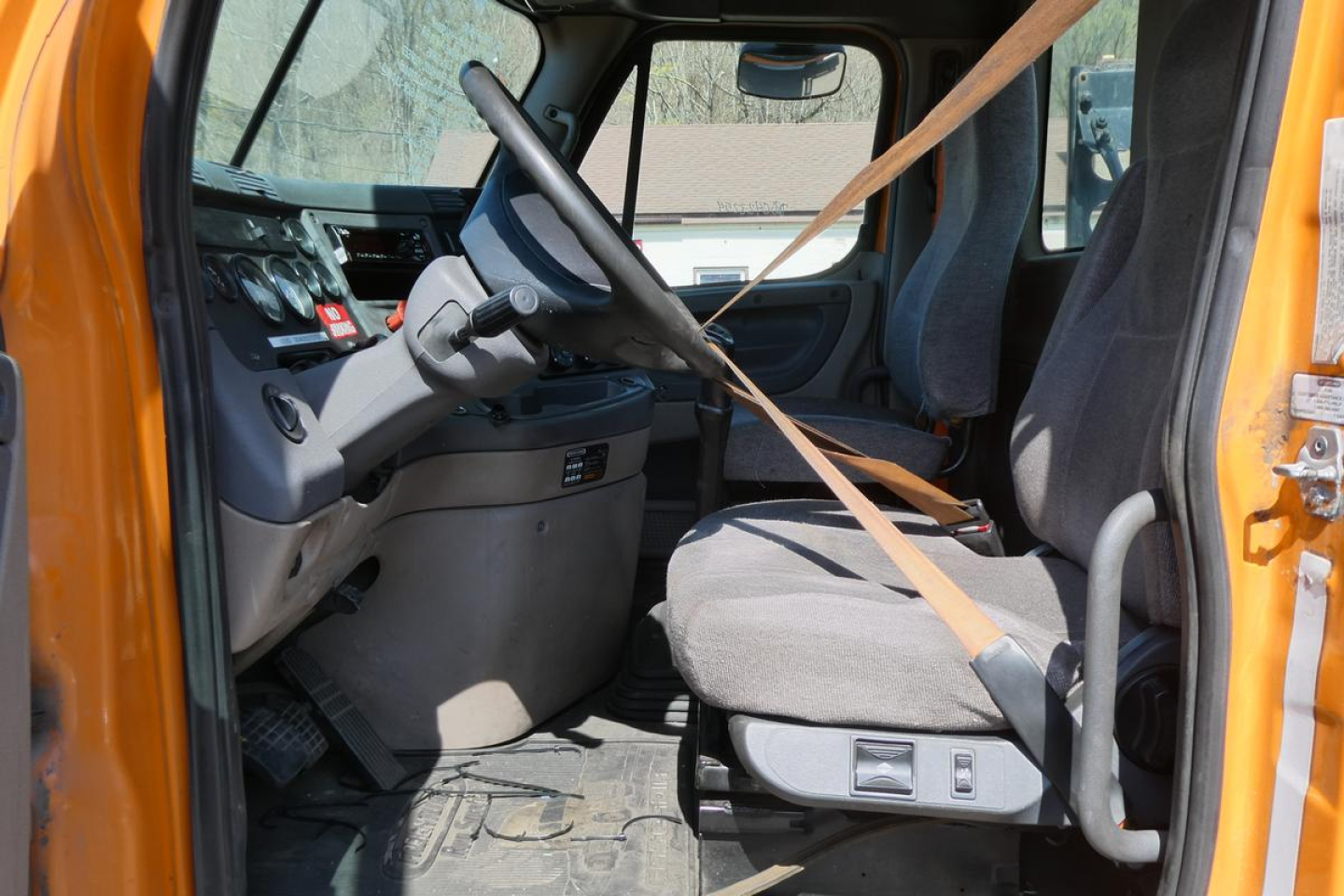 Truck cab interior of a 2013 Freightliner Cascadia 125 daycab showing steering wheel, driver's seat, dashboard, and seat belt in view.