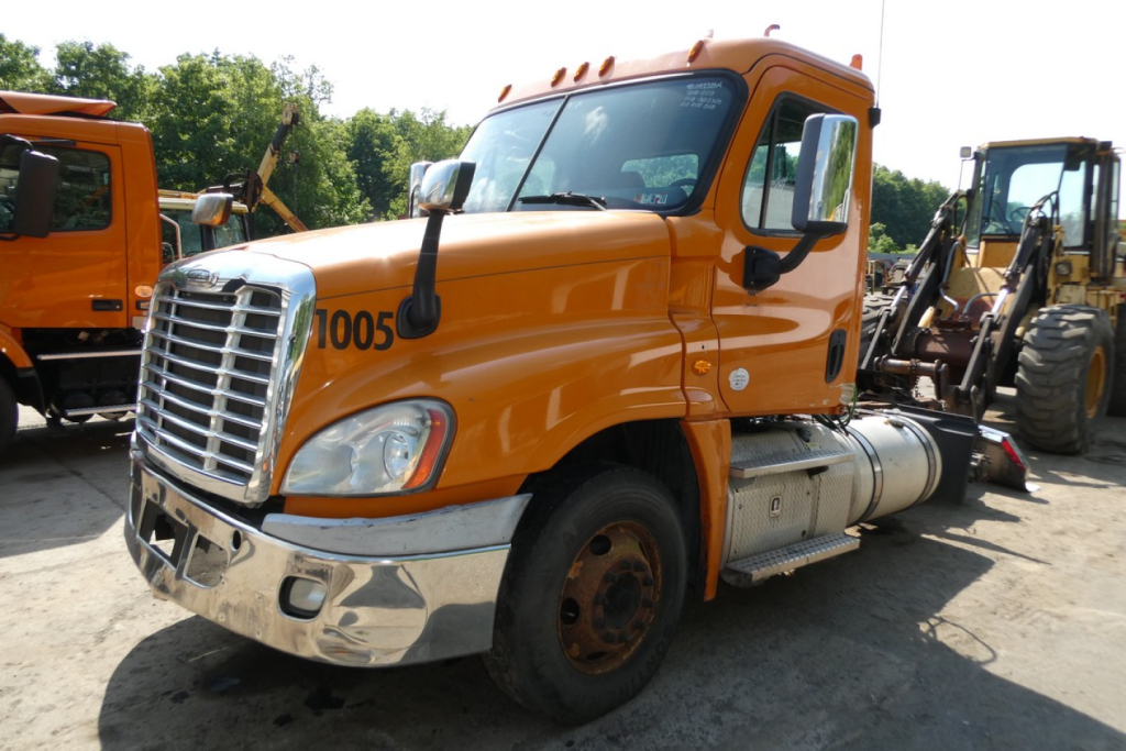 Orange Freightliner Cascadia 125 Daycab truck in a lot showing front grille and side; number 1005 on door; chrome bumper; fuel tank and steps visible.