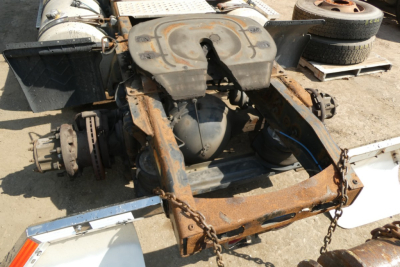 Tractor-trailer chassis with rusted frame and exposed rear axle, Freightliner Cascadia components visible on a flatbed, wheel and chain shackles in view.