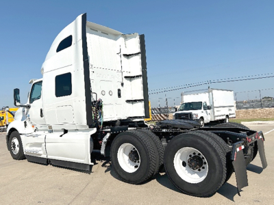 Truck sleeper cab chassis with dual rear axles and white paint. Visible are large fuel tanks, rear wheels, and the cab with a high-roof sleeper. No legible labels readable on the body.