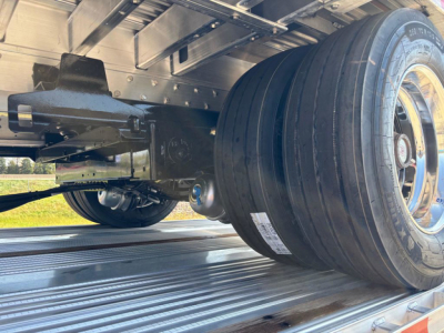 Trailer undercarriage with dual wheels and suspension, black frame, metal deck surface visible, tire tread and wheel rim details.