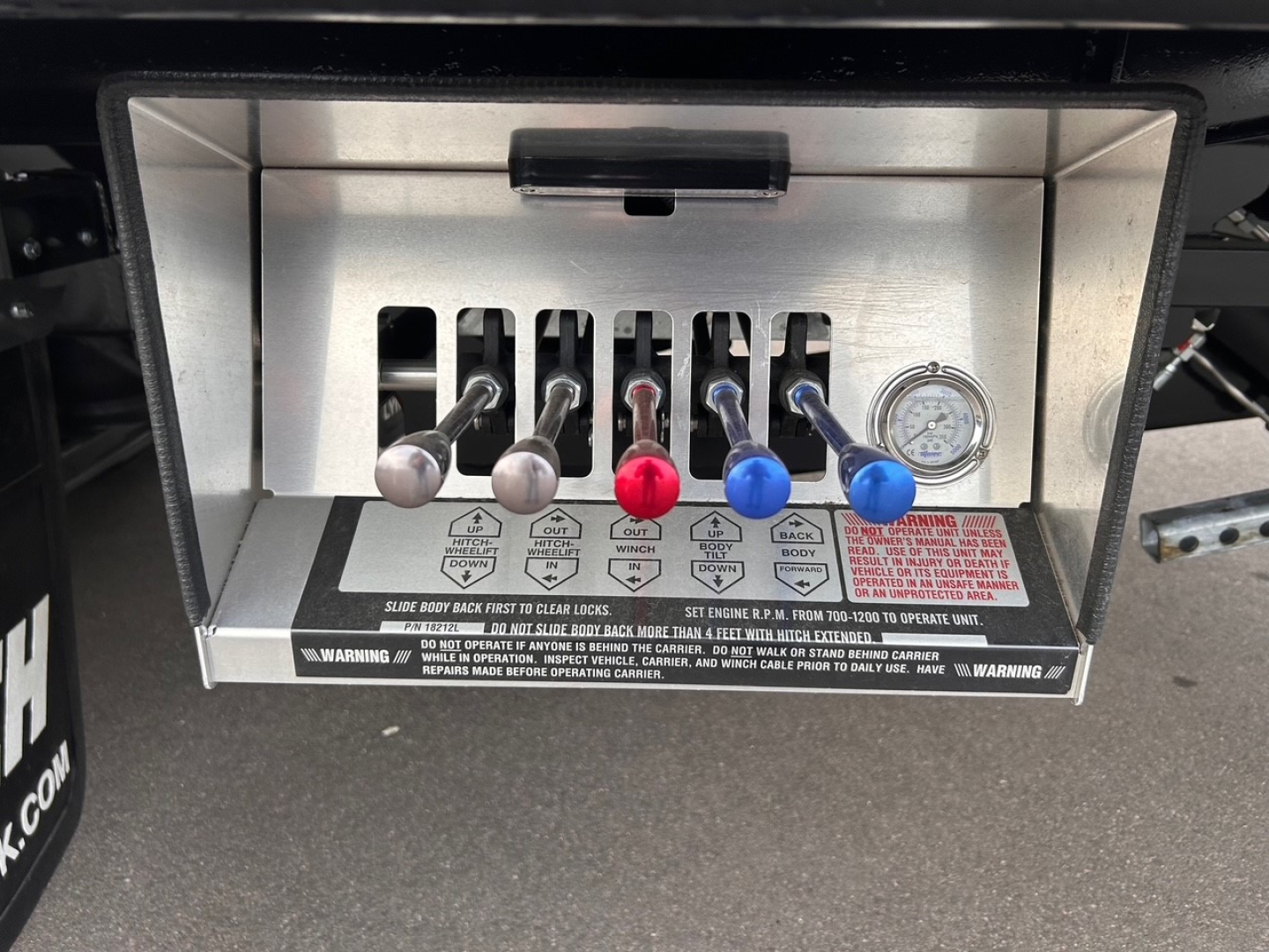 Truck control panel with six levers labeled and a dial gauge on the right. See red, blue, and silver levers and warning labels below the levers.