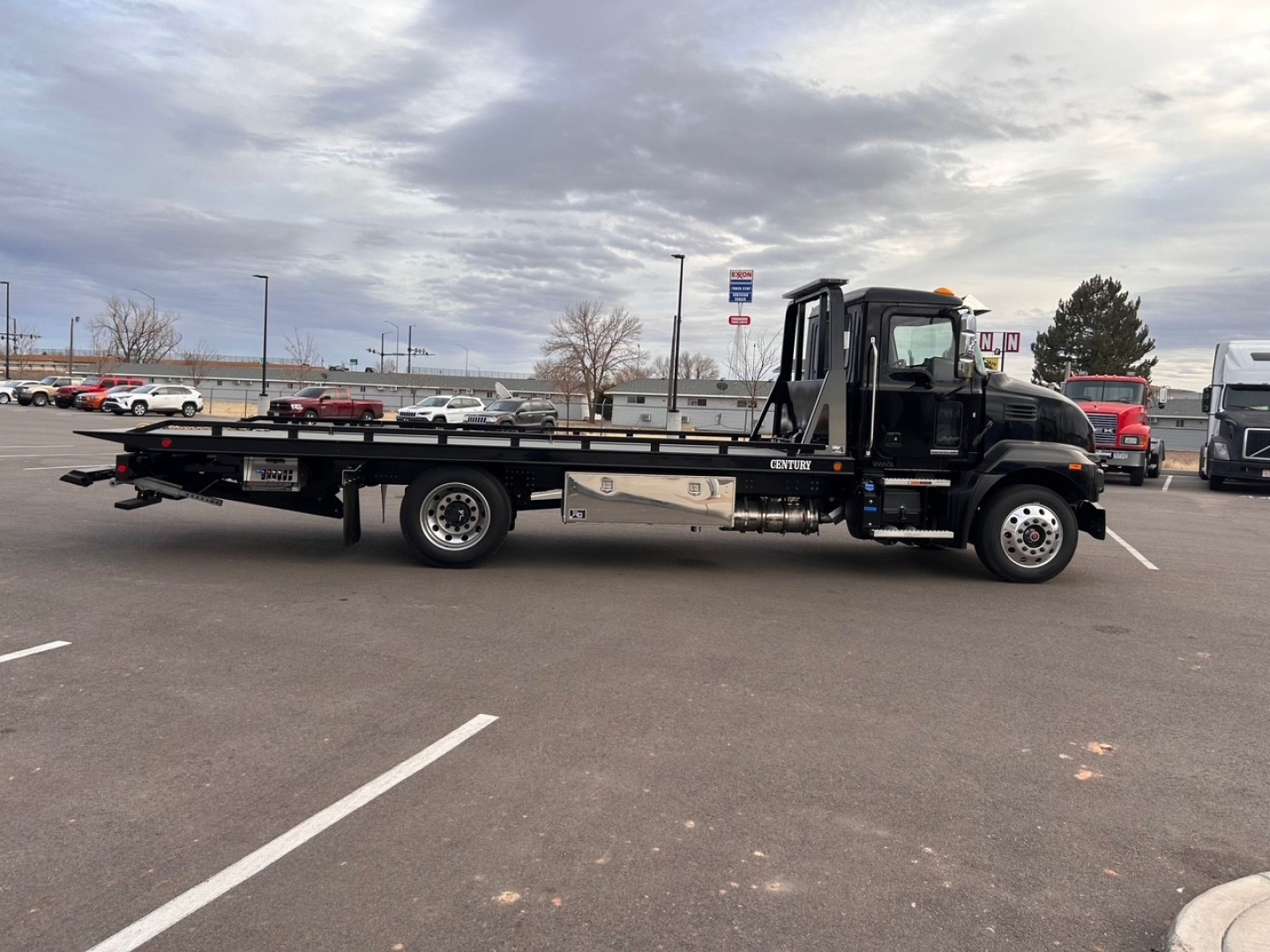 Flatbed tow truck in profile view showing long lowbed deck and black cab with chrome details.