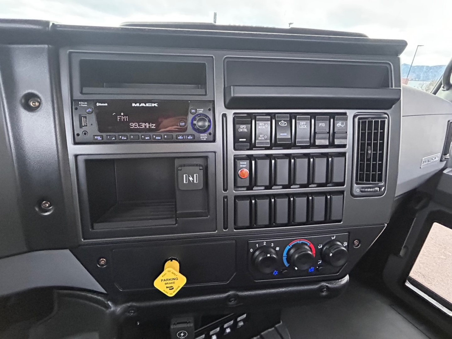 Mack MD6 dashboard showing radio unit, multiple toggle switches, air conditioner controls, and a yellow tow-pin in lower panel.