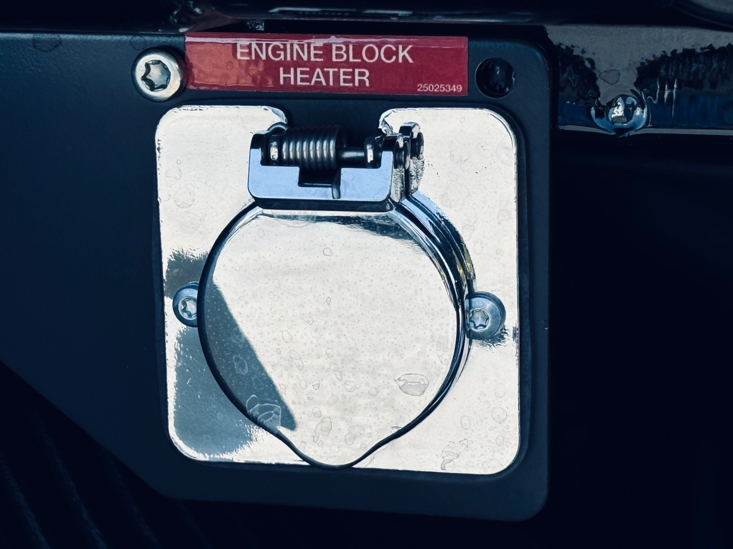 Mack MD6 engine bay component showing a chrome fuel cap/cover labeled Engine Block Heater with red tag, mounted on a metallic panel.