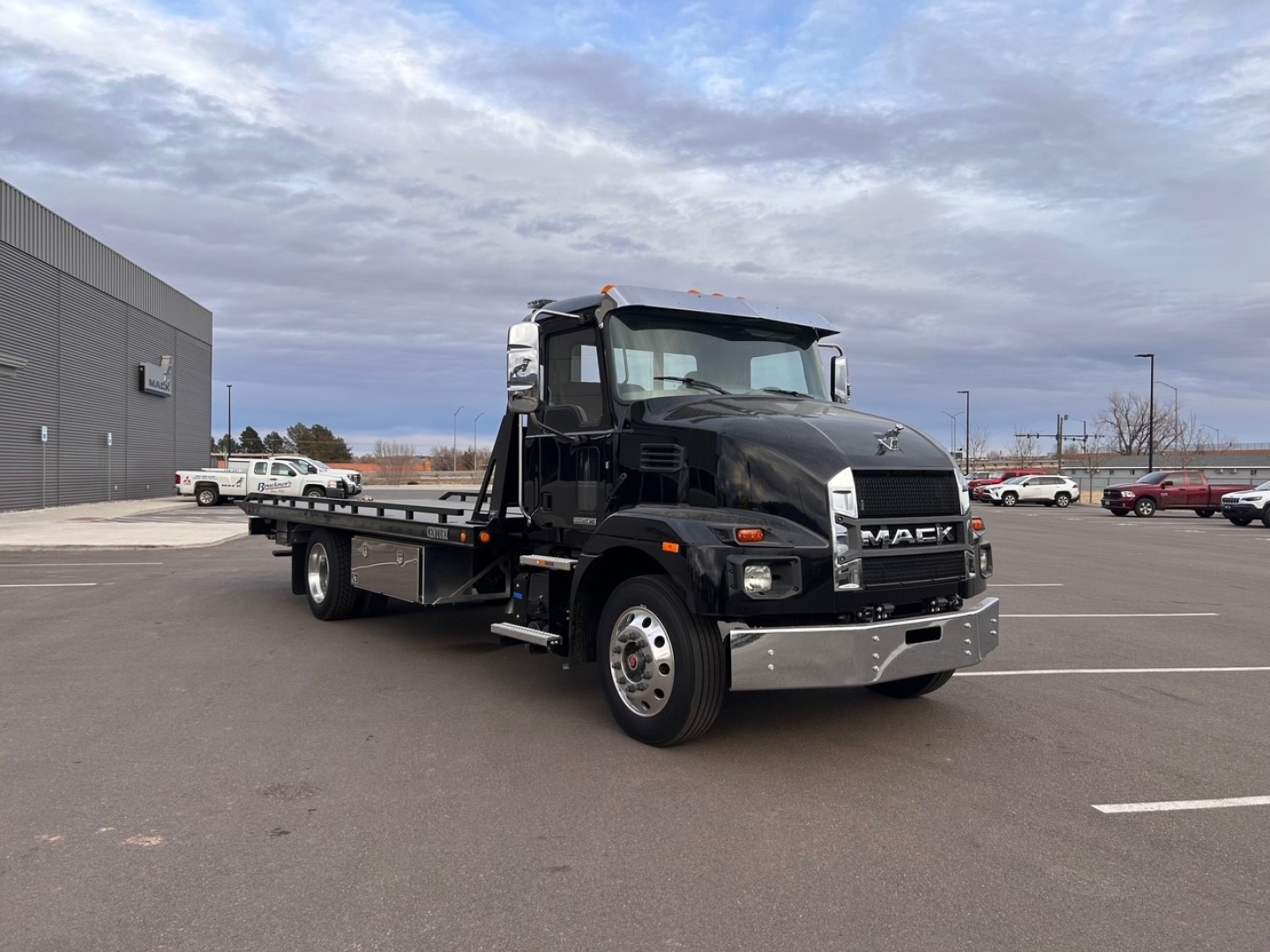 Tow truck: 2025 Mack MD6 cab with flatbed, front view showing black exterior, chrome bumper, and side mirrors; VIN placard area not legible.