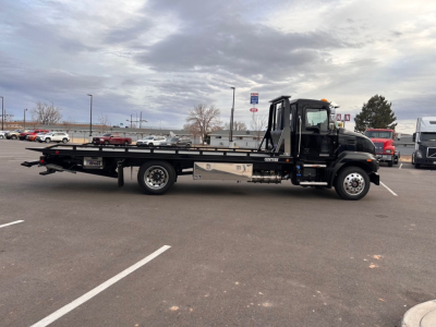 Flatbed tow truck in profile view showing long lowbed deck and black cab with chrome details.