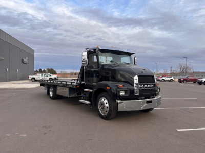 Tow truck: 2025 Mack MD6 cab with flatbed, front view showing black exterior, chrome bumper, and side mirrors; VIN placard area not legible.