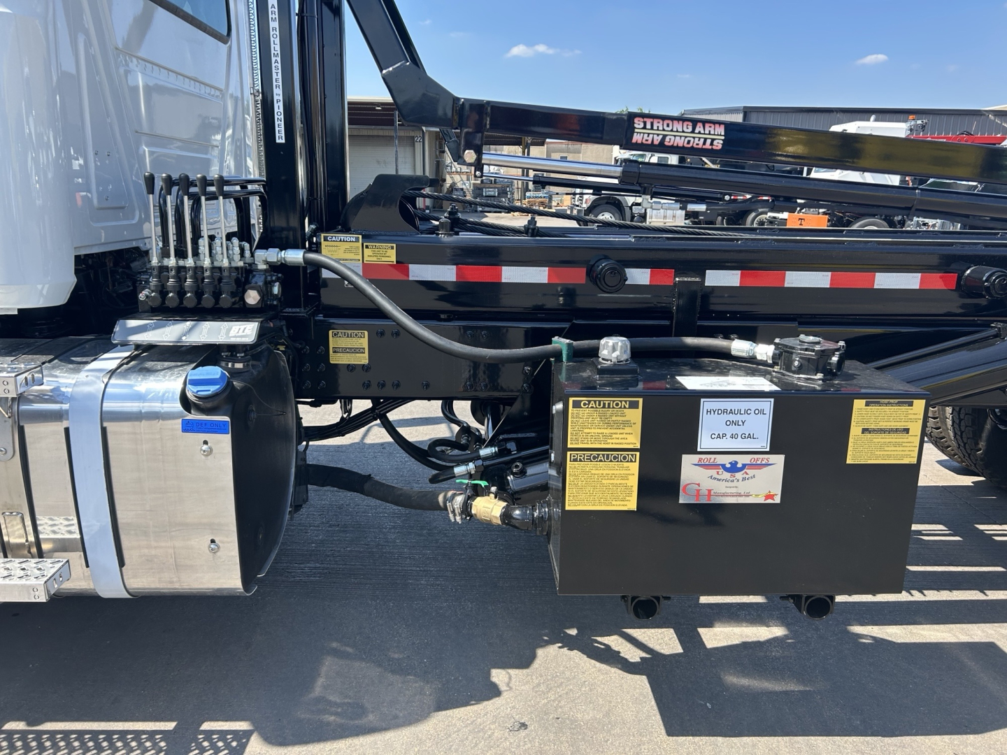 Front side of 2026 Mack GR64B roll-off truck showing hydraulic reservoir, battery box, and warning labels with VIN plate visible.