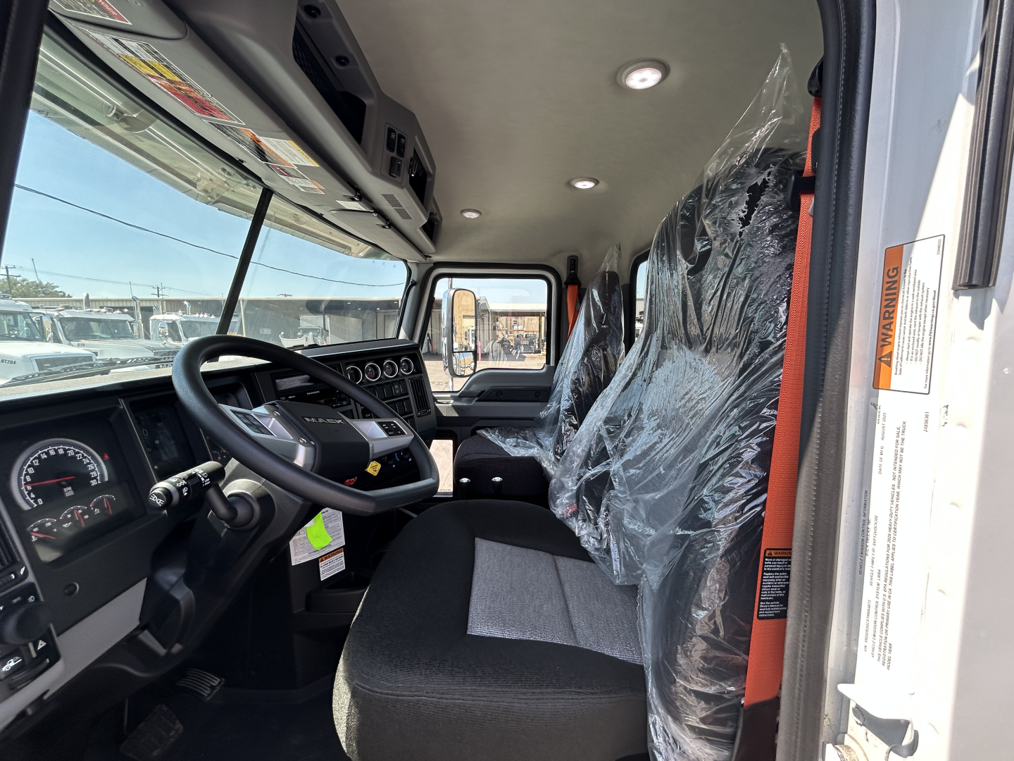 Interior of a new Mack GR64B roll-off truck cabin showing steering wheel, dashboard with gauges, and plastic-covered seats.