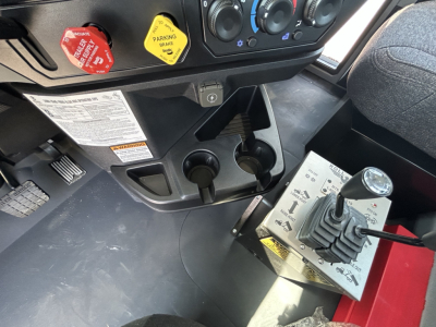 Cab interior of 2026 Mack GR64B rollover truck showing gear shifter panel, two cup holders, parking brake lever, and control switches with labeled decals.