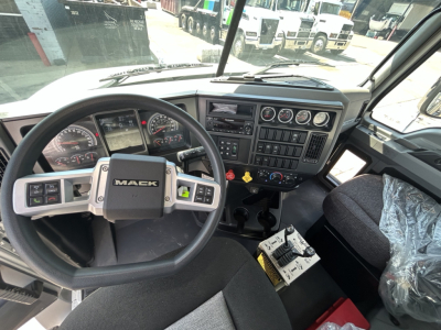 Mack GR64B truck cockpit showing steering wheel, dashboard gauges, and control panel with switches.