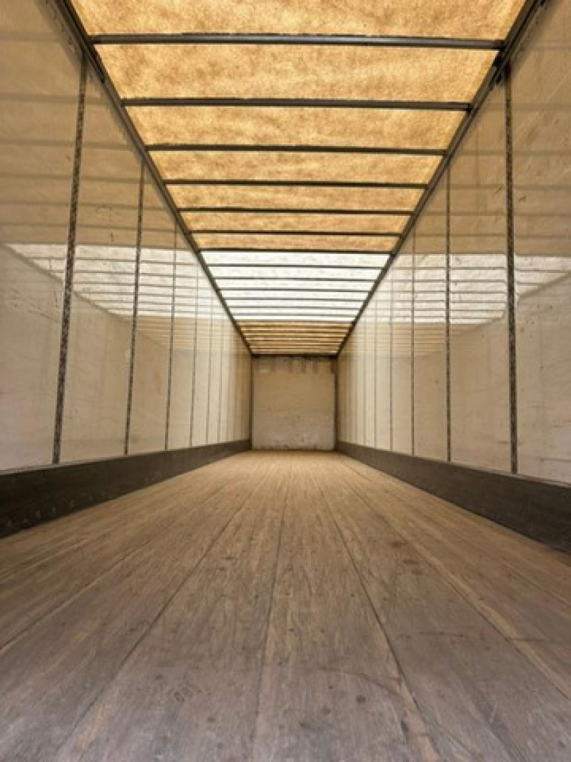 Trailer interior showing empty wood floor with metal sidewalls and ceiling ribs in a long rectangular box trailer.