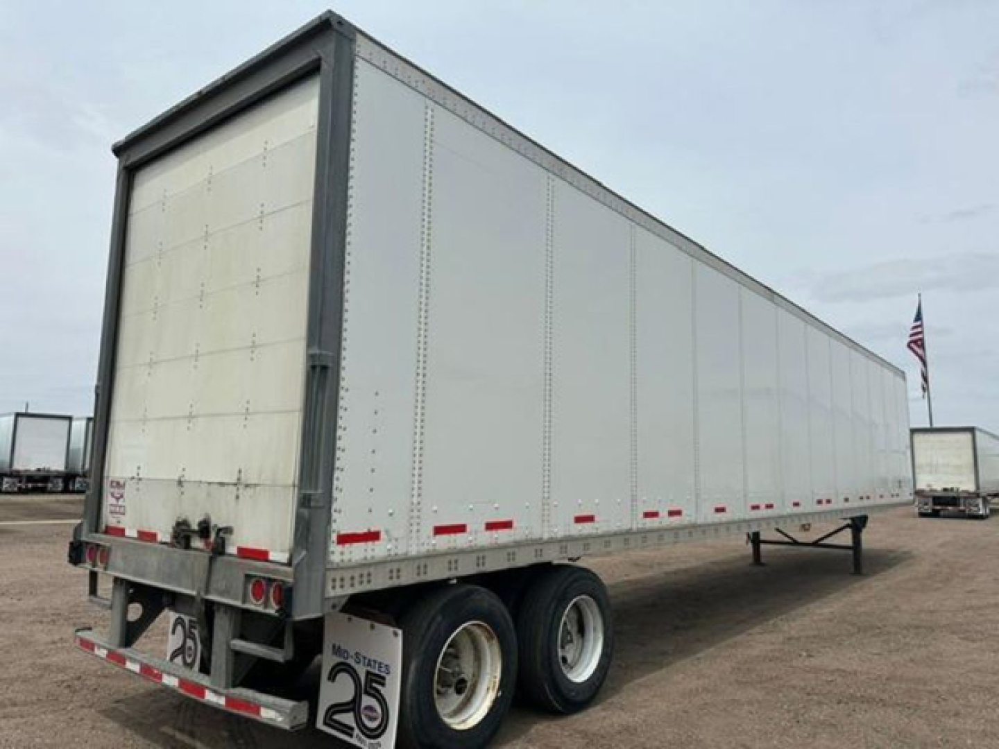 2016 Wabash van trailer showing side panels, rear doors, and dual axle with tires. Visible labels include small red and white reflective markings along the lower edge and rear with a number plate and trailer frame.