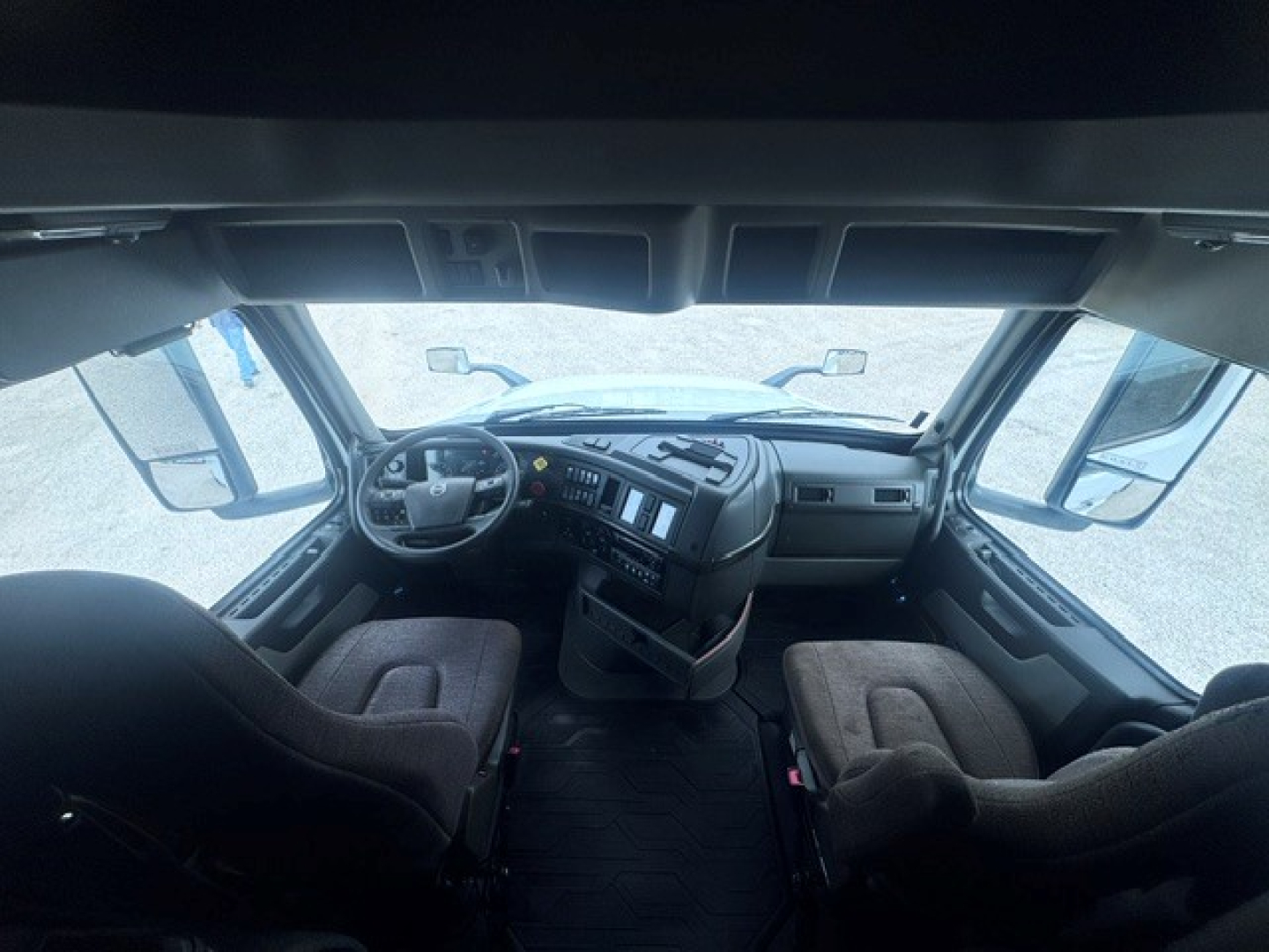Cab interior of a Volvo truck with two seats, dashboard, steering wheel, and large windshield visible.