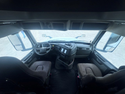 Cab interior of a Volvo truck with two seats, dashboard, steering wheel, and large windshield visible.