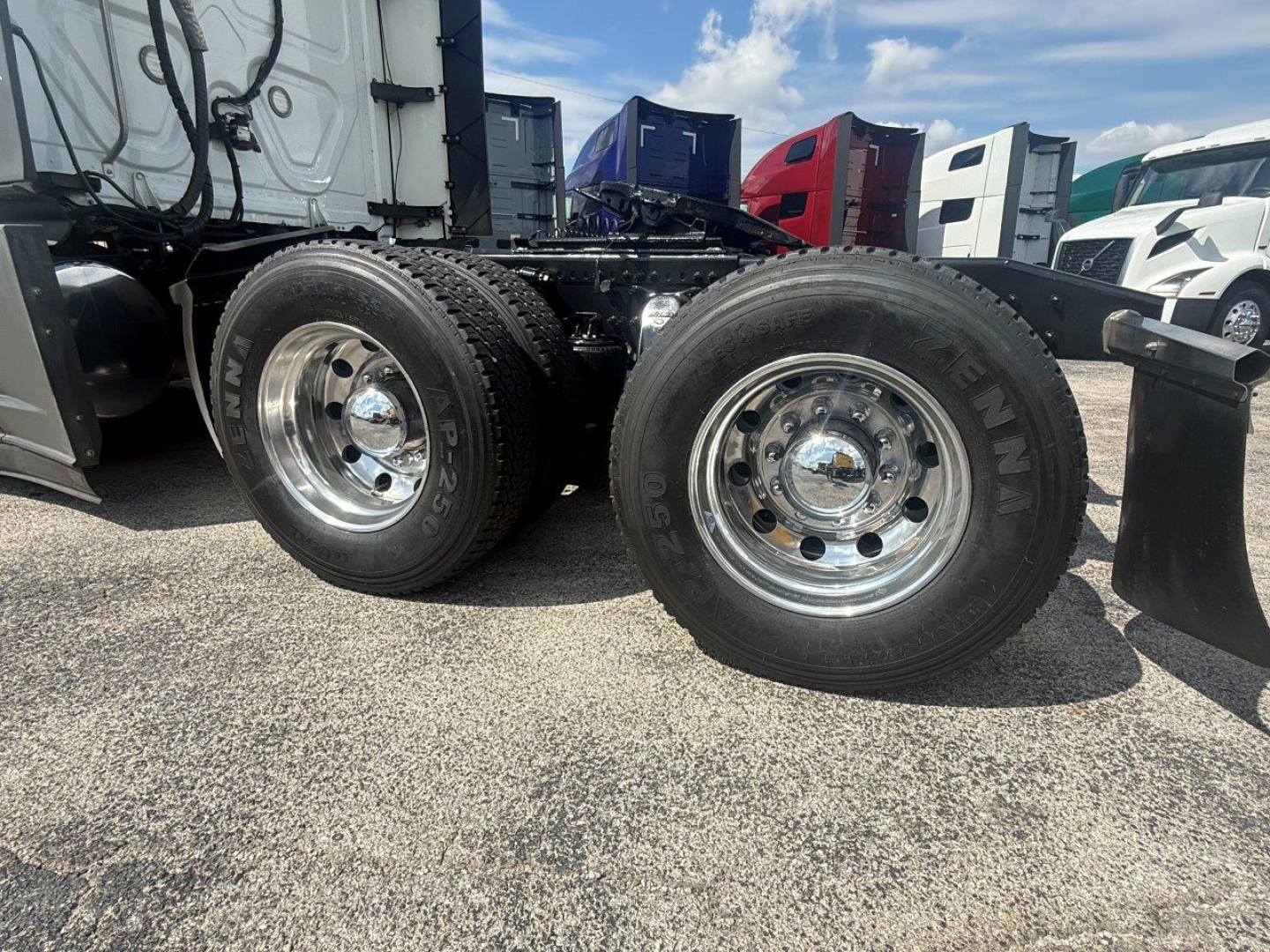 Freightliner Cascadia 126 tractor rear view showing dual rear axles with chrome wheels and tires, fuel tank area, and part of the sleeper cab in a truck lot.