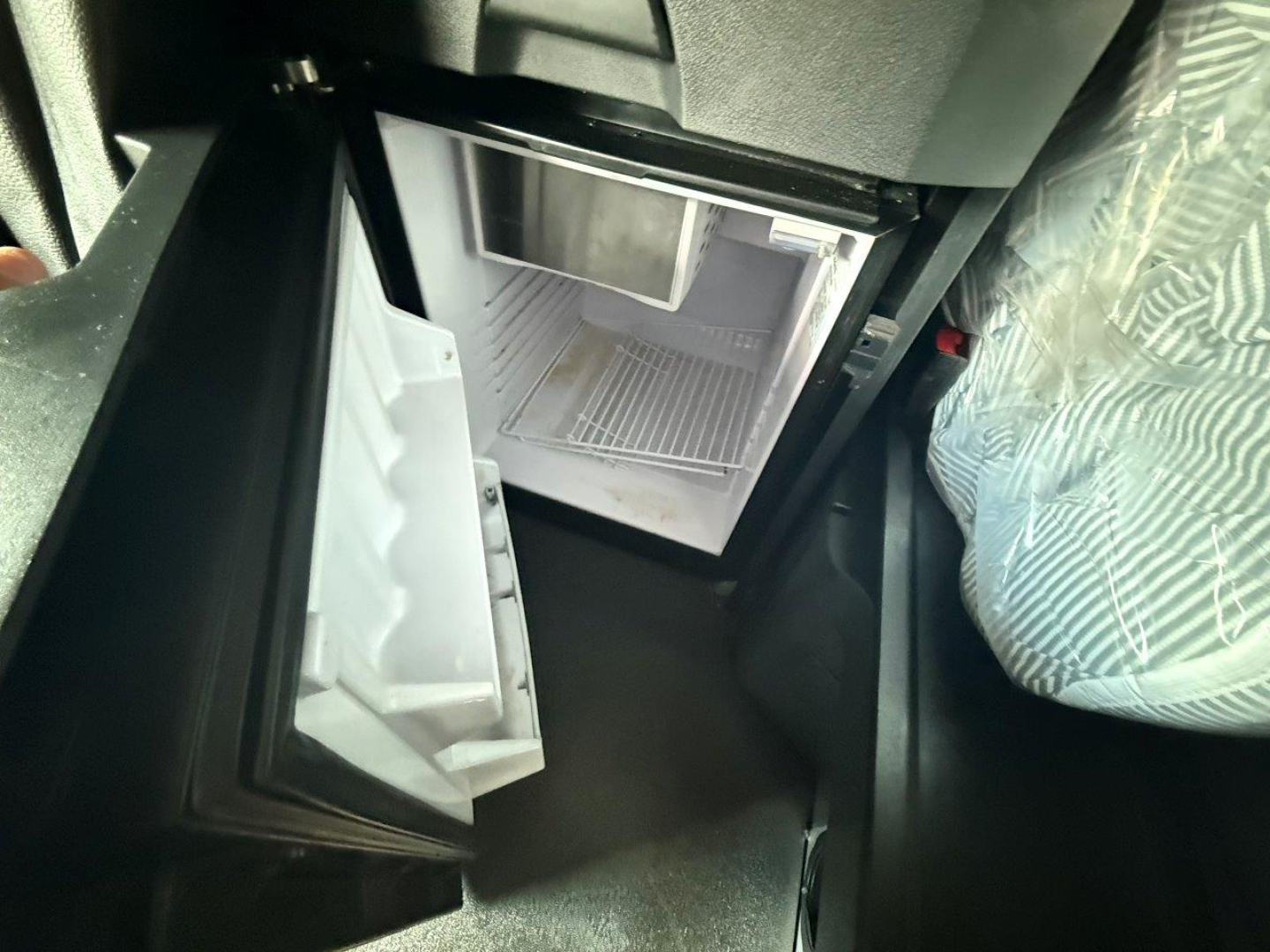 Cabin area showing a small under-dash refrigerator with open door and freezer shelf.