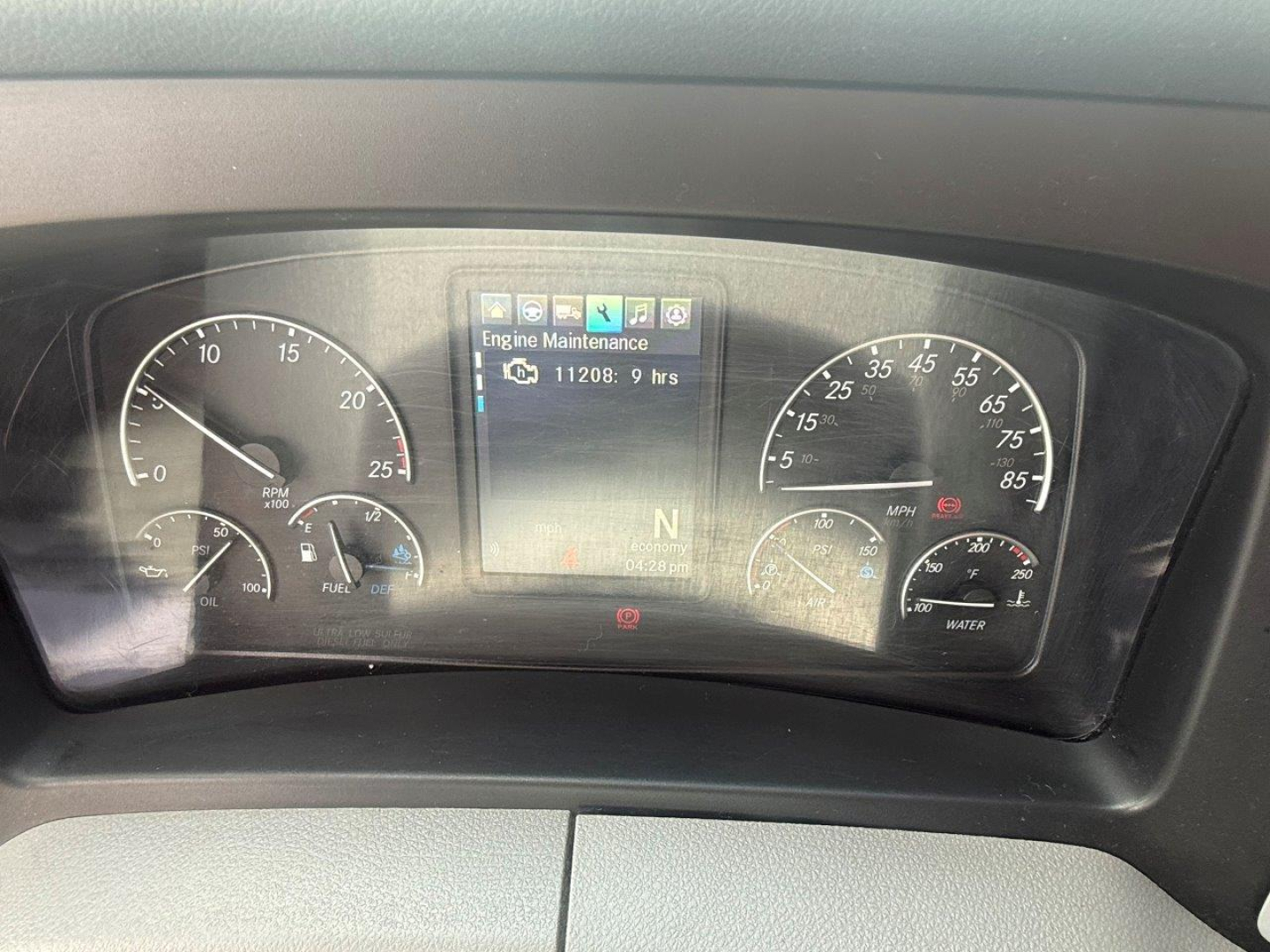 Dashboard cluster of a Freightliner Cascadia 126 showing instrument gauges and center display, with a navigation-like screen reading Engine Maintenance and 11208.9 hrs.