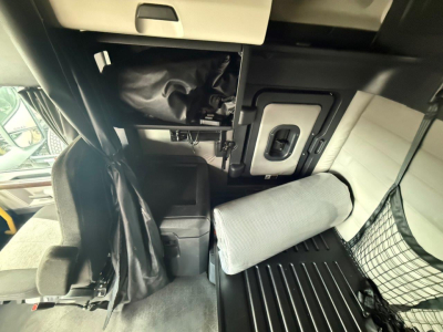 Cab interior of a Freightliner Cascadia 126 showing sleeper area with back of seat, overhead storage, mesh net, and a folded gray cushion.