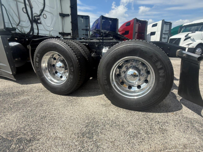 Freightliner Cascadia 126 tractor rear view showing dual rear axles with chrome wheels and tires, fuel tank area, and part of the sleeper cab in a truck lot.