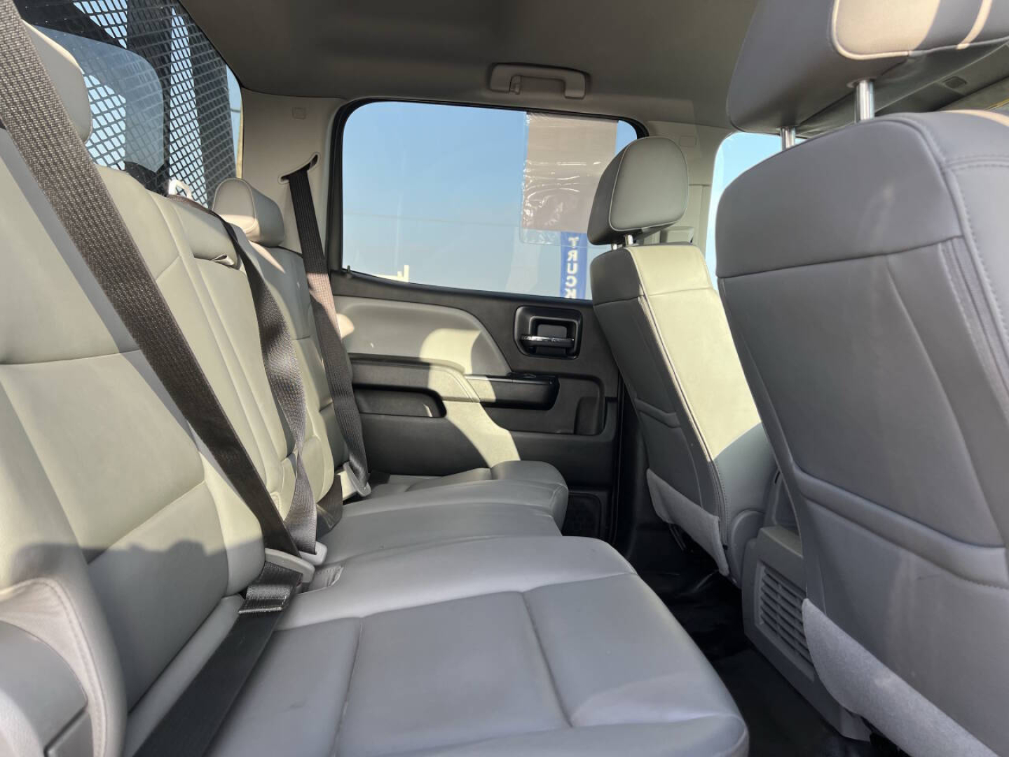 Chevrolet Silverado interior rear seat view showing light gray fabric seats, rear door, and center console; three-row? front seats visible; seat belts and cabin trim.