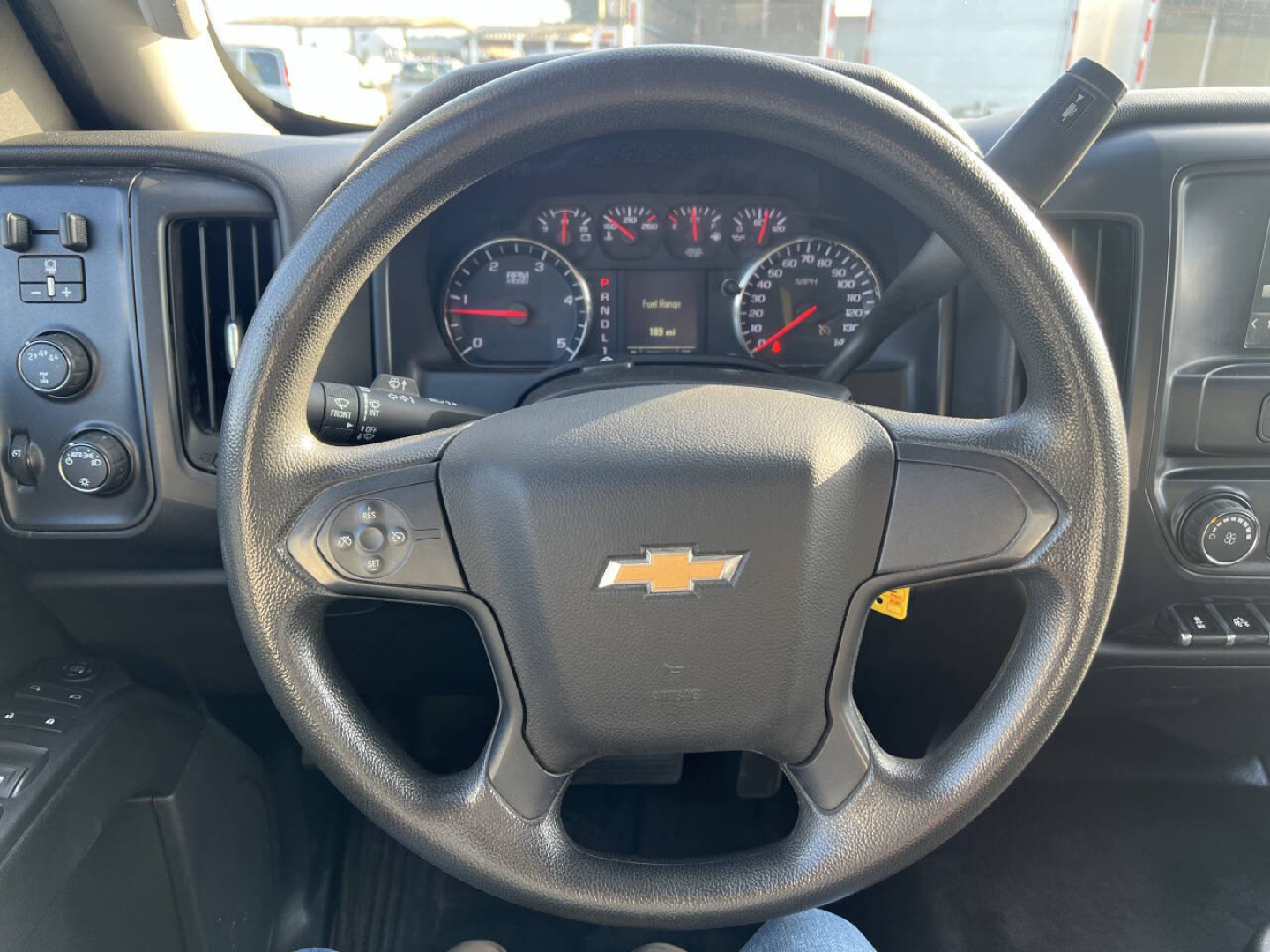 Chevrolet Silverado steering wheel and instrument cluster in the dash view. Center of steering wheel shows Chevrolet bowtie logo; gauges and digital display visible behind wheel.