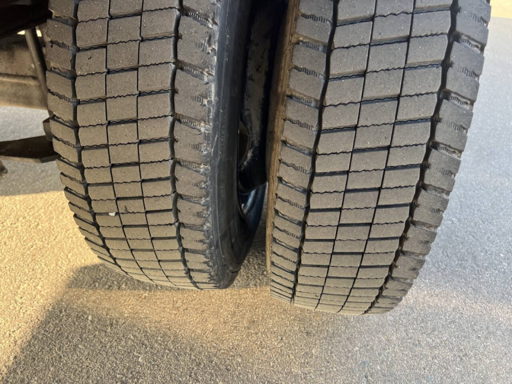 Two truck tires side by side with deep tread pattern, flatbed truck wheel assembly visible.