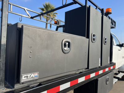Flatbed truck with large black tool/storage boxes mounted on the bed, CT A logo, white cab in background, orange beacon on top, side view showing storage compartments and rails.