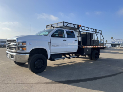 Truck bed with crane rack on a white 2022 Chevrolet Silverado flatbed utility truck, side view showing dual rear wheels and steel framework installed over bed