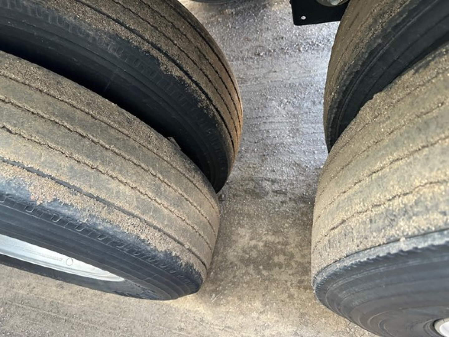 Trailer axle wheels showing dual rear tires with dirt and grime on tread surface in a hopper trailer.