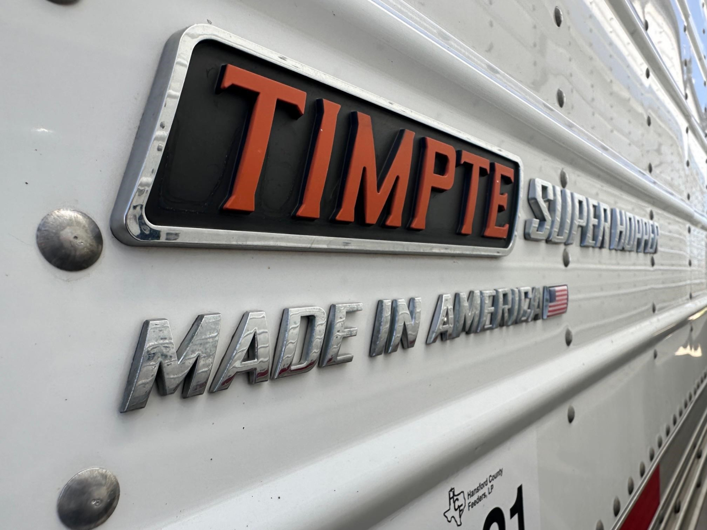 Trailer side angle showing TIMPTE SUPER HOPPERS badge and MADE IN AMERICA lettering on a white trailer.