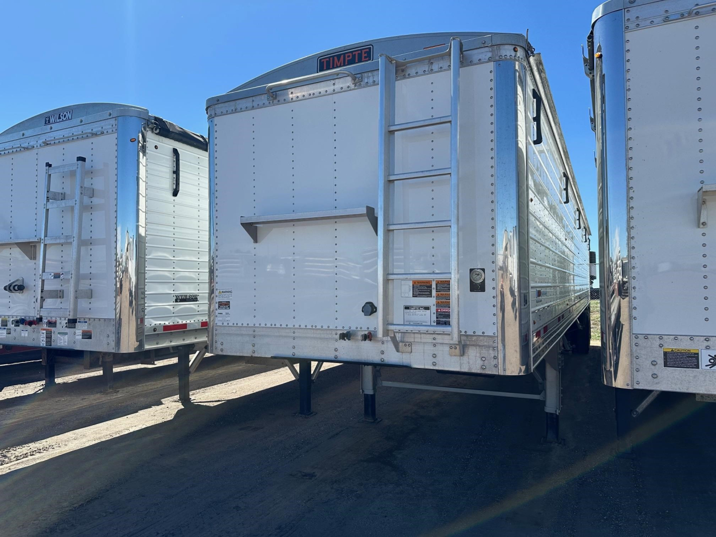 Timpte Super Hopper trailer rear view showing fold-down ladder and hitch, metal paneling, and landing gear.