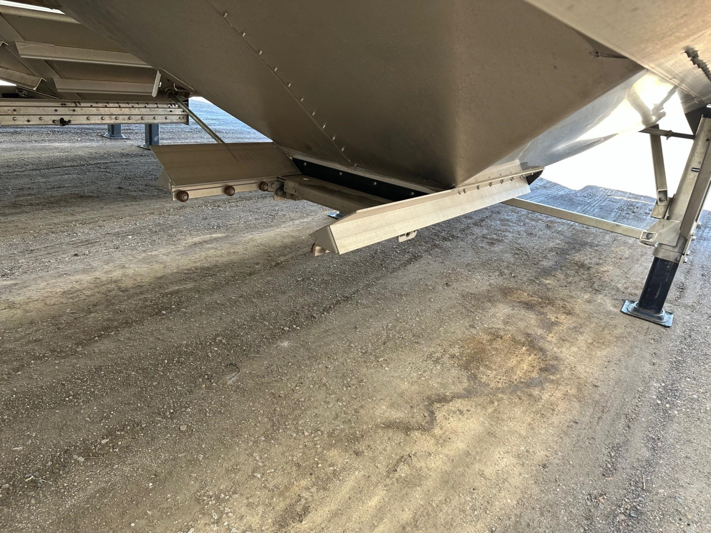 Trailer undercarriage showing a metal framework and support legs with a feeds side step and sliding mechanism near the hopper.