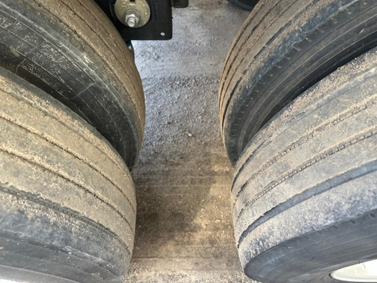 Trailer wheel area showing dual large tires and suspension attachment; dusty surface visible between tires.