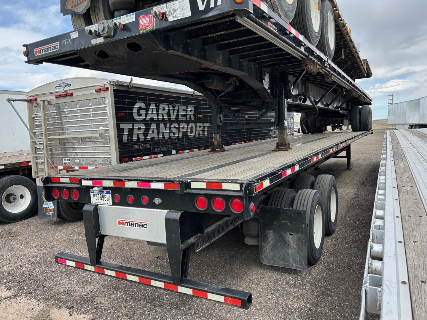Manac 48' extendable steel flatbed trailer with a loaded heavy equipment at rear; dual tandem axles, hydraulic extendable chassis visible, Garver Transport branding on tool cage, reflective tape along edges.