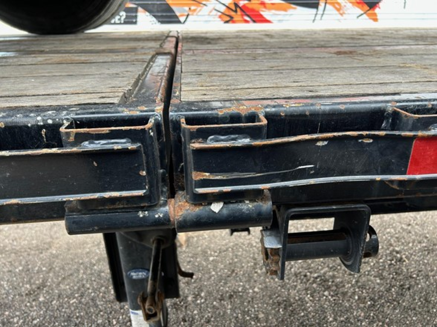 Manac extendable steel flatbed trailer rear hitch area showing coupler and platform edge with wear marks.