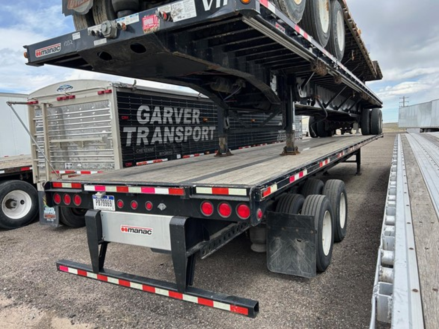 Manac extendable steel flatbed trailer with a load of a semi-truck on top, Garver Transport branding, rear view showing multiple axles and taillights