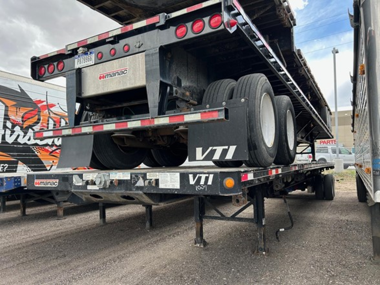 Manac extendable steel flatbed trailer with rear extendable deck and dual rear axles; VTI branding on side and rear, rear lights, and metal support legs visible
