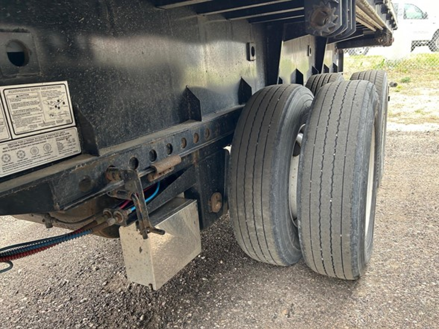 Manac extendable steel flatbed trailer underside showing dual rear axle tires and warning labels