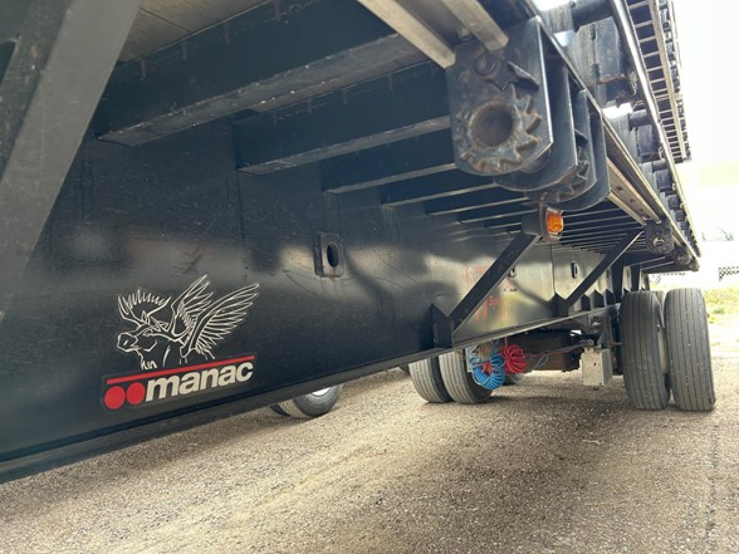 Manac extendable steel flatbed trailer side view showing Manac logo and underside structure.